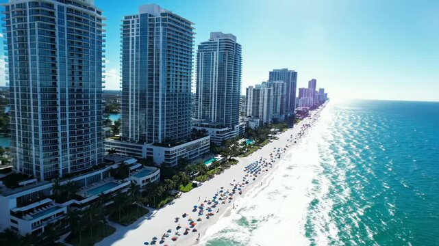 Aerial view of luxury highrise condominium buildings overlooking a crowded white sand beach and turquoise ocean water 4k video