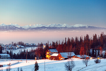 snowy mountain village at dawn with snow-covered homes, forest, and ridge under soft sunrise