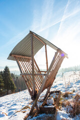 Rustic wooden hay feeder on snowy hill in Gorce mountains under bright winter sky