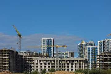 Fototapeta premium Construction cranes and new buildings, construction work of modern skyscrapers on a sunny day.