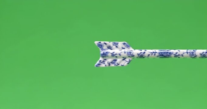 Ceramic arrow decoration with blue and white floral pattern against a bright green screen background