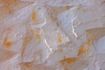 Close-up of textured stucco wall with carved geometric shapes and warm ochre stains, rough surface detail providing natural abstract background for design work.