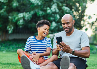 Portrait of father and son having fun using a mobile phone outdoors in park or nature,, family...