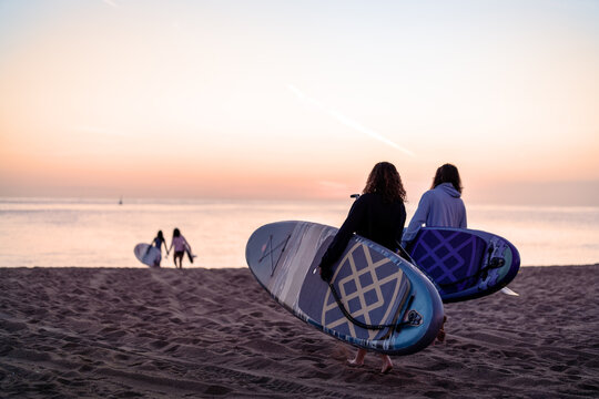 Friends share a joyful moment at the beach during sunset, holding vibrant surfboards while laughing - Powered by Adobe