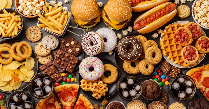 Vibrant assortment of fast food items such as fries, burgers, onion rings, soft drinks, pizza, and sugary desserts arranged in a full, energetic composition that celebrates guilty pleasures.