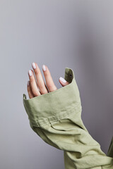 Woman’s hand with soft white manicure gripping the cuff of a light green denim jacket against a neutral grey background