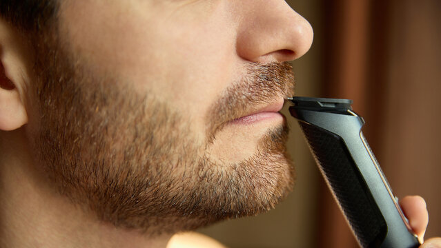 Precise mustache trimming using electric shaver. Concept of grooming editorials, men blogs, shaving-device branding, accurate detailing, clean maintenance visuals.