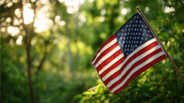 American flag waving on a pole with bright sunlight filtering through green trees