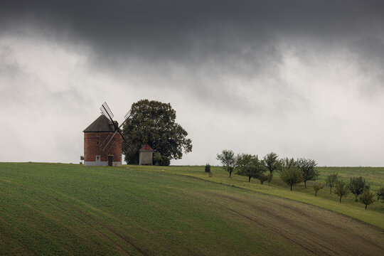 View of a brick windmill, a verdant field, and a row of trees under a moody sky, creating a captivating landscape, Brno, South Moravian Region, Czechia.