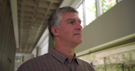 Middle aged man glancing to the side with subtle smile in modern office hallway thoughtful relaxed and optimistic expression in professional environment