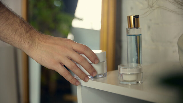 Hand reaching for skincare cream on bathroom shelf. Concept of beauty brands, packaging design, morning routines, wellness communication, home-care aesthetics for men grooming. - Powered by Adobe