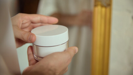 Man holding skincare cream jar during calm morning routine. Concept of male grooming brands, daily self-care visuals, wellness content, product education and relaxed lifestyle imagery.