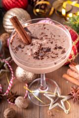 Spiced chocolate eggnog martini cocktail, served with cinnamon stick, sprinkle of nutmeg and chocolate, on cozy Christmas background 