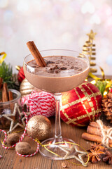 Spiced chocolate eggnog martini cocktail, served with cinnamon stick, sprinkle of nutmeg and chocolate, on cozy Christmas background 