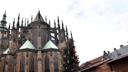 St. Vitus Cathedral in Prague Castle, Czech Republic, with a decorated Christmas tree and market stalls in the foreground during winter.