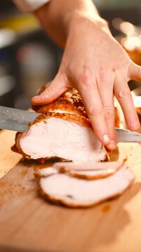 A person is cutting a piece of meat on a wooden cutting board. The knife is very sharp and the meat is sliced into thin pieces