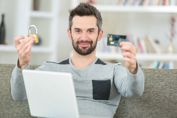 man using laptop at home holding padlock and bank card
