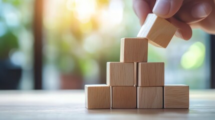 A hand stacks wooden blocks in a warm, sunlit environment, symbolizing creativity, construction, and playful learning.