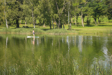 Une femme sur un paddle sur un lac. Balade en paddle l'&eacute;t&eacute;. Sport aquatique. Loisir sur un lac en &eacute;t&eacute;. Vacances vers un &eacute;tang