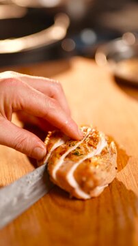 A person is cutting a piece of meat on a wooden cutting board. The knife is being used to slice the meat into thin strips