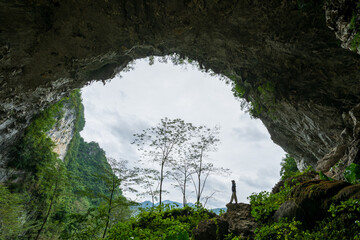 Silhouette of Hiker Standing at Massive Cave Entrance Overlooking Karst Mountain Landscape in China