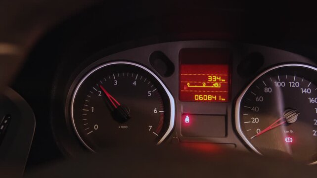 Car's dashboard with the tachometer needle rising as the engine starts and warning lights illuminating
