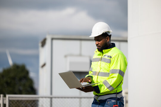 African Engineer man working on tablet computer in field with wind turbines background, Windmill. environmental renewable clean energy. Wind power generation. Windmill engineer inspection progress