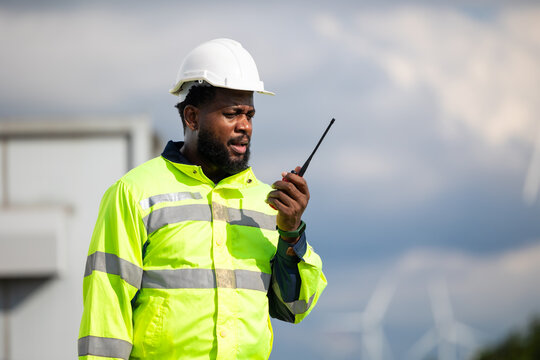 African Engineer man working on tablet computer in field with wind turbines background, Windmill. environmental renewable clean energy. Wind power generation. Windmill engineer inspection progress