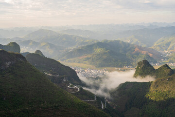 Mountain Town Nestled in Valley With Drifting Clouds and Winding Roads in Guangxi China