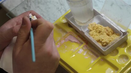 Dental technician applying primer on dental mold model using brush for prosthetics, laboratory tools, dentistry education, prosthodontics, oral restoration.