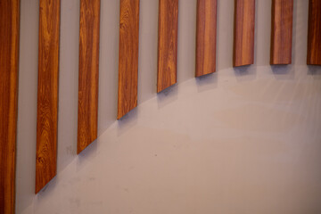 Obraz premium Architectural pattern of brown wooden vertical slats with diagonal cuts at the bottom right, creating a boundary with a blank beige wall space