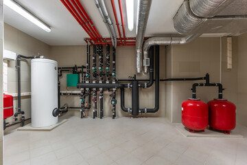 Bright and clean utility room showcasing a modern plumbing and heating system. Red pipes, tanks,...