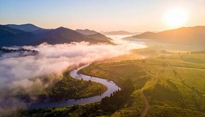 Aerial view of a river winding through a valley, surrounded by mountains and a layer of fog, illuminated by the warm light of sunrise.