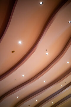 Low angle view of a smooth, wavy peach pink-toned modern ceiling with recessed spotlights, creating a soft, warm, and dynamic pattern