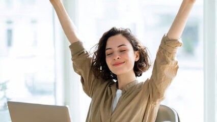 Young woman celebrating success at desk in bright office laptop open positive work environment