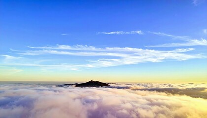 A mountain peak rises above a sea of clouds, bathed in the warm light of a sunset under a clear blue sky.
