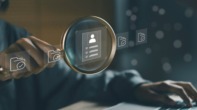 Hand holding magnifying glass over digital document icons, symbolizing document management, HR process automation, and job recruitment systems for modern business workflow and data organization.