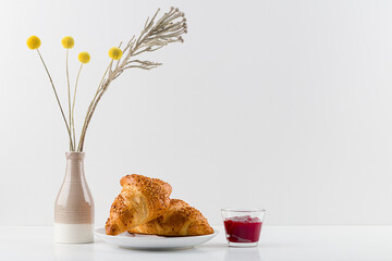 Croissant and a mug on a wooden stand, a vase , white background. minimalism. Copy space,