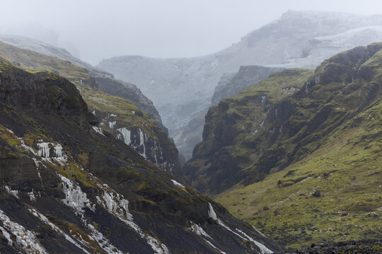 View of steep, moss-covered slopes descend into a misty gorge, creating a dramatic landscape of contrasting textures and colors, Golden Circle, Rangarbing eystra, Iceland.