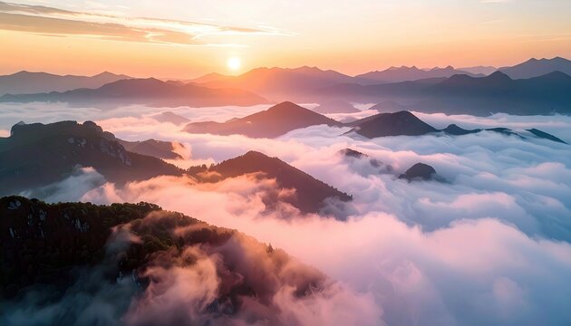 A scenic landscape photograph of mountains partially covered in fog and clouds at sunrise. The sky is a warm orange and pink, creating a peaceful atmosphere.