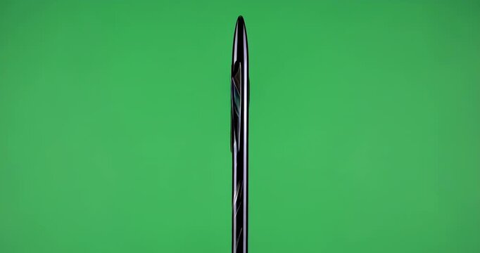 Close up of the tip of a black pen with a silver clip against a bright green screen background