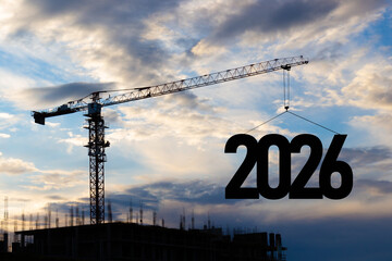 2026 New Year for planning and strategies concept background. Silhouette of a construction crane at a construction site raising the number 2026 year to blue sky. Ideas of development and investment