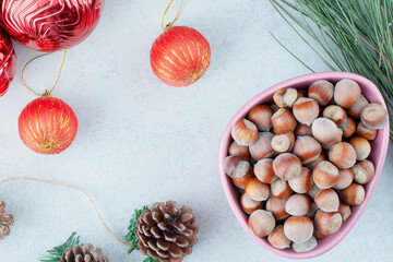 Christmas Hazelnuts in Pink Bowl with Red Baubles and Pine Cones on White Surface