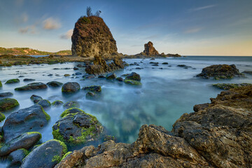 View of mossy rocks meet the tranquil sea beneath a majestic rock formation under a serene sky, Yogyakarta, Special Region of Yogyakarta, Indonesia.