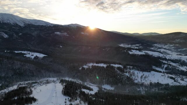 Time lapse of winter sunset over snow-covered mountains, showcasing gradual light changes and atmospheric shifts, with a smooth camera pan revealing the serene landscape.