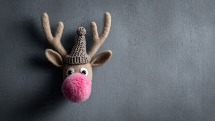 A festive plush reindeer head, wearing a knit hat, with a prominent pink fluffy nose, against a textured grey background.