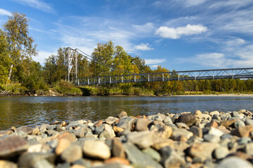River pebbles autumn forest landscape blue sky sunshine background suspension bridge Sweden