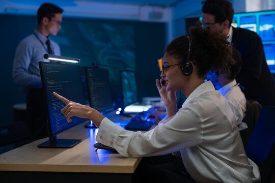 Diverse team of professionals customer service agent wearing headsets and monitoring computer working in dark control room. Female support and assistance call center at night in modern office.