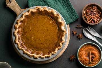 Top view of classic pumpkin pie with spices and ingredients arranged around