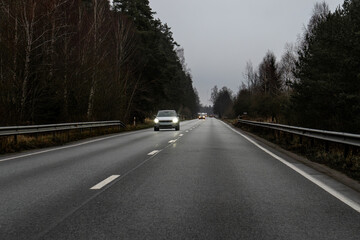 Car Driving on Wet Asphalt Road Through Forest on a Gloomy Winter Day